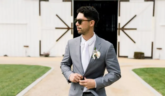 Men's summer blazer wedding outfit with light gray jacket and white pants.
